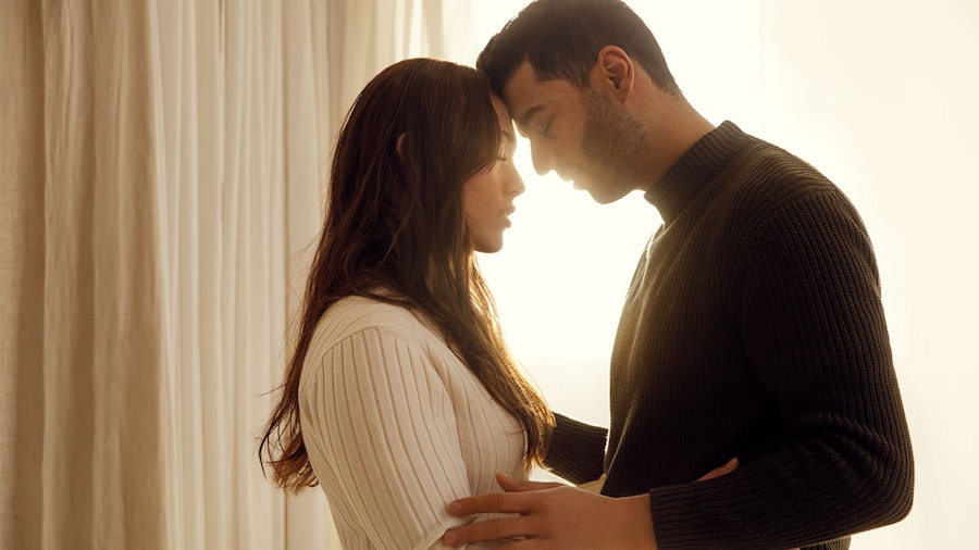 Couple standing in glowing window touching foreheads