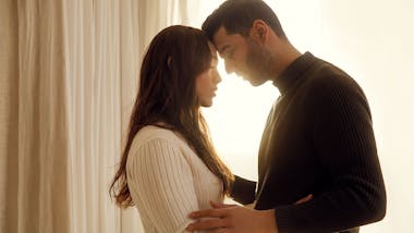 Couple standing in glowing window touching foreheads
