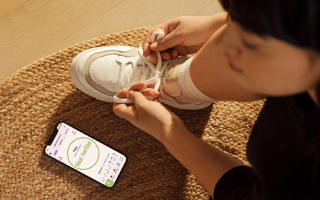 Woman tying her shoe with the Natural Cycles app open on her phone next to her.