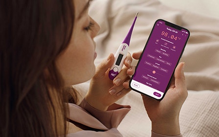 Woman adding her temperature to the Natural Cycles app while holding a thermometer in her other hand.