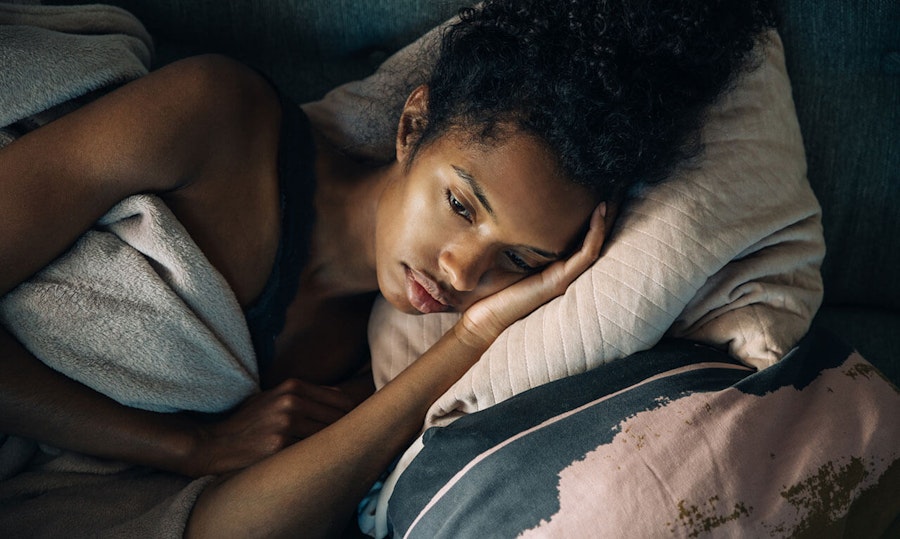Woman looking down lying on her side with her hand to her head