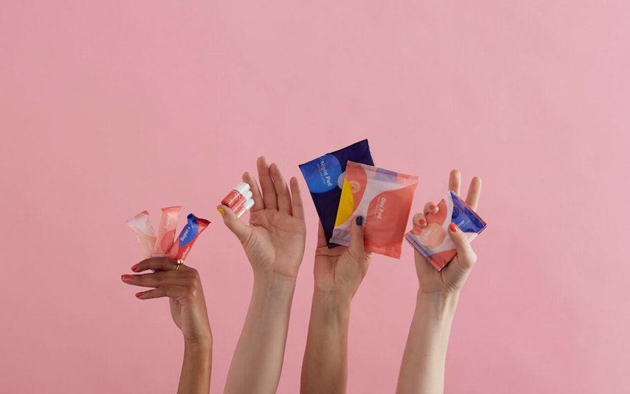 Four hands holding Callaly's period products against an empty pink background. From left to right: tampliners, tampons, pads and liners.