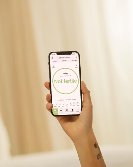 a hand holding a phone with the natural cycles app