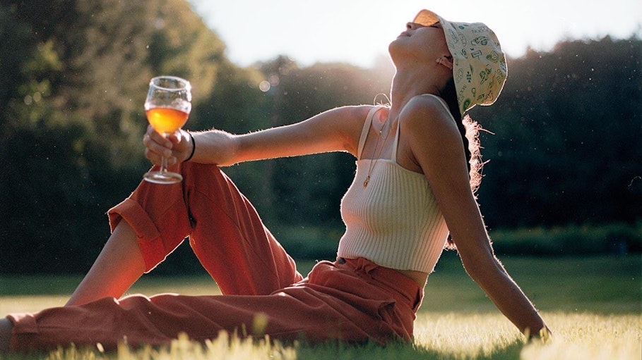 Sav sits on the grass in the sun holding a wine glass