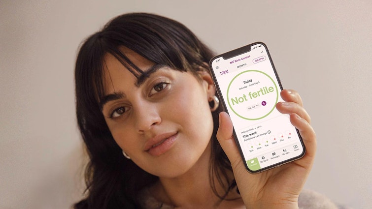 Photograph of woman holding up a phone with a screen showing 'not fertile' while half smiling at the camera