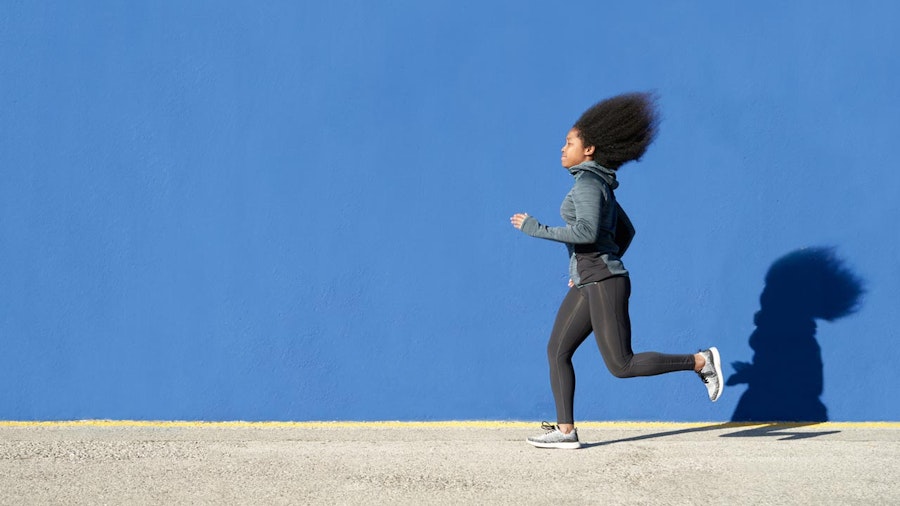 Photograph of a woman running alongside a bright blue wall