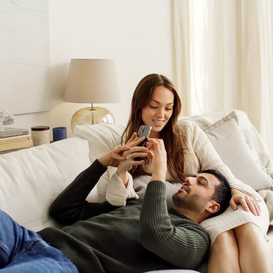 Couple in bed looking at thermometer and fertility app on phone