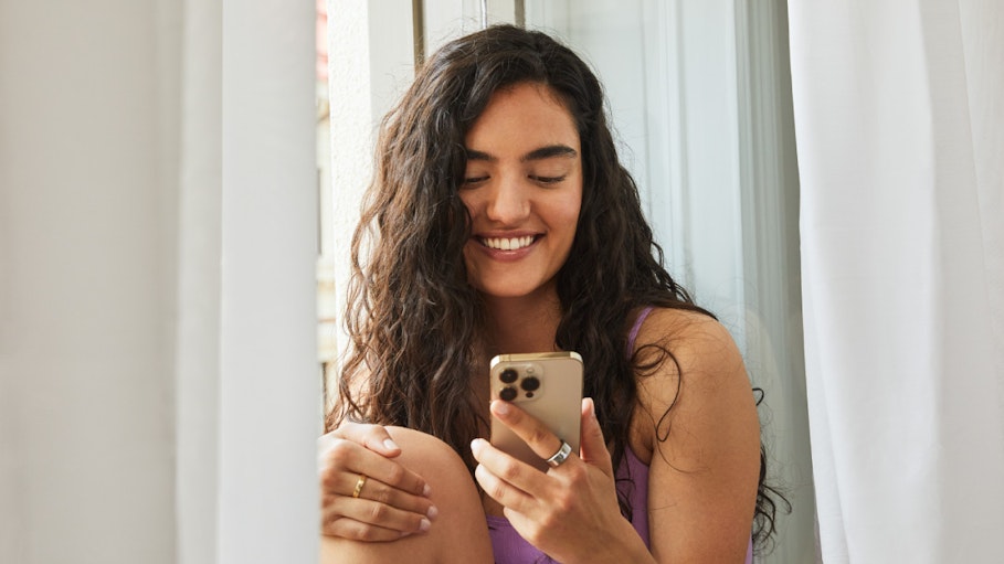 Smiling woman looking at phone wearing Oura Ring