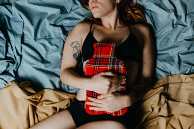 Woman in bed holding tartan hot water bottle to her stomach