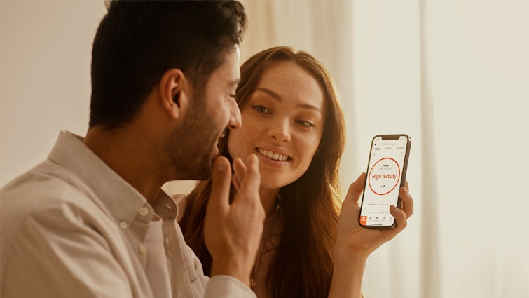 Couple smiling, looking at phone screen that says 'high fertility'