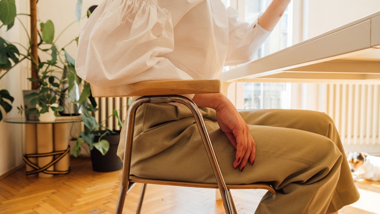 Woman sat at a desk only visible from the neckdown in a sunny apartment