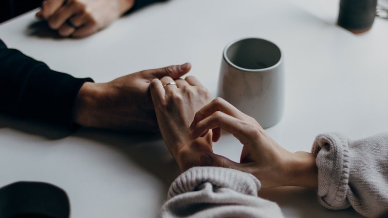 Two people holding hands over a table next to a coffee cup