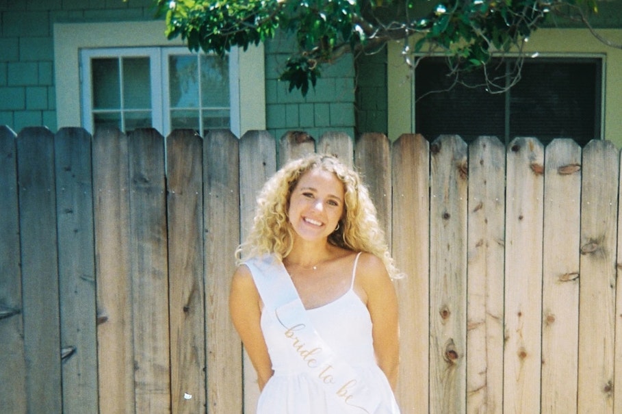 Aeva standing in front of fence in white dress