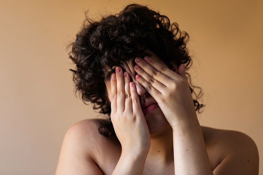 Person with dark curly hair covering their face