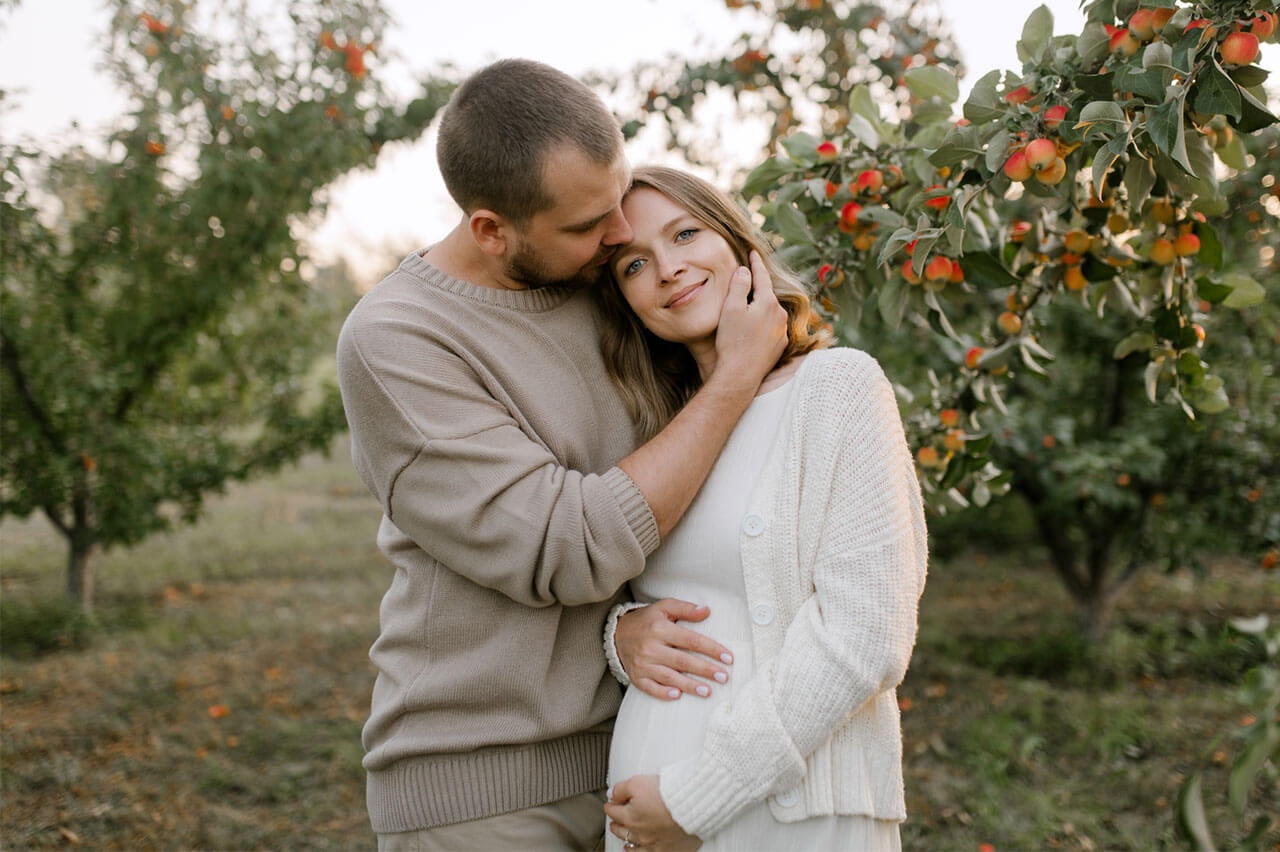 Pregnant couple standing in an orchard