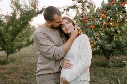 Pregnant couple standing in an orchard
