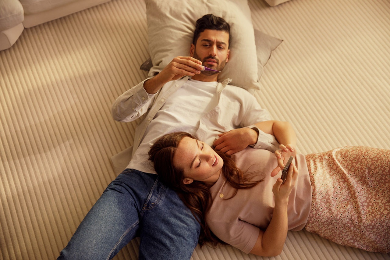 Couple lying on the floor, man looking at thermometer