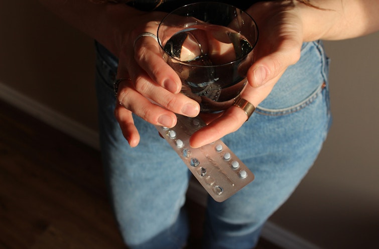 Photo of a woman's hands holding a glass of water and a packet of birth control pills