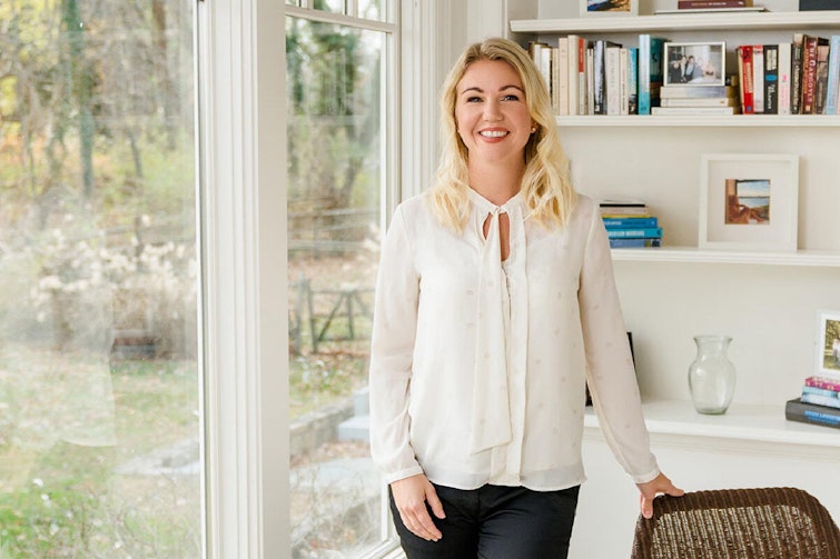 Elina Berglund Scherwitzl standing in front of a bookcase, wearing white and smiling