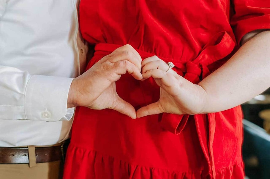 Erin and her husband making a heart sign with their hands against Erin's body