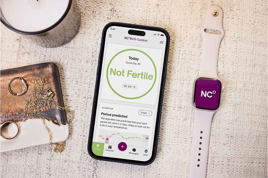 Apple Watch on a table displaying the NC logo next to a phone showing the text 'not fertile'