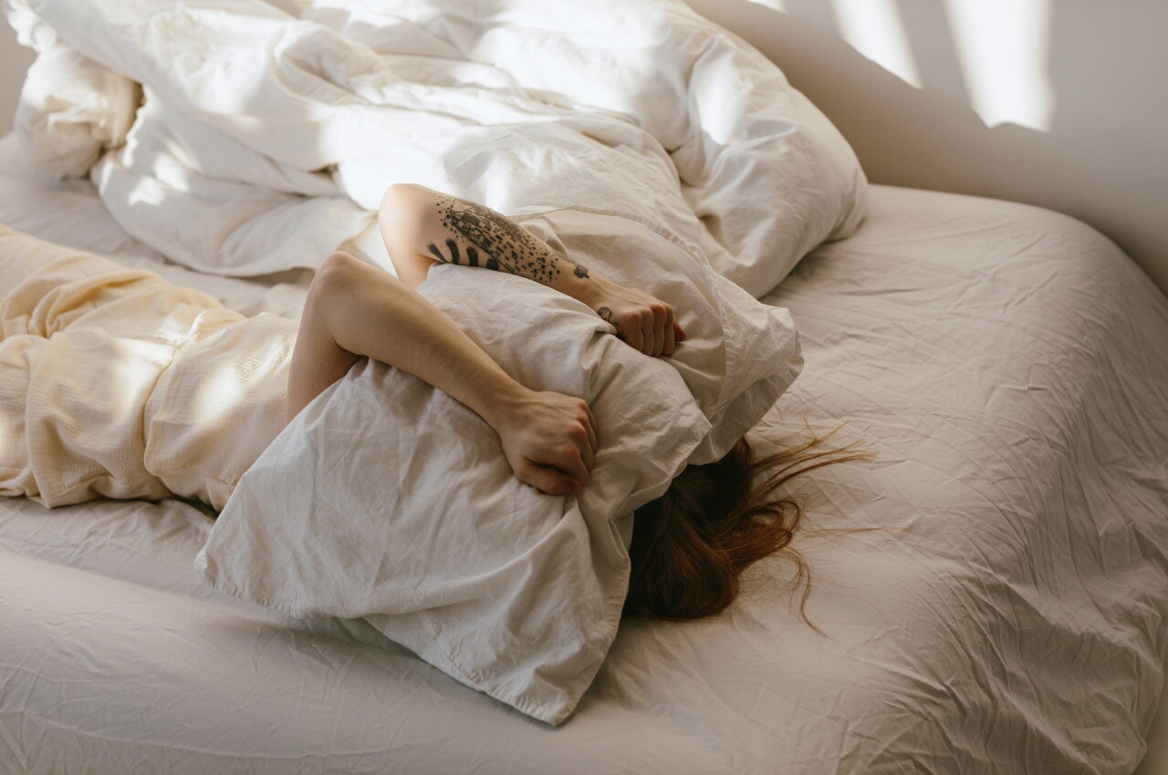 Woman lying in bed with a pillow pulled over her head