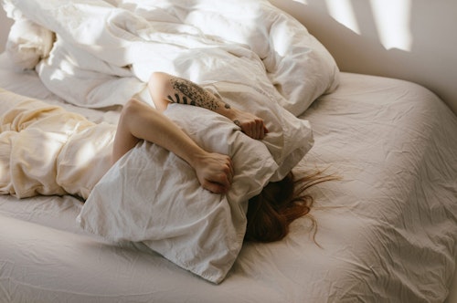 Woman lying in bed with a pillow pulled over her head