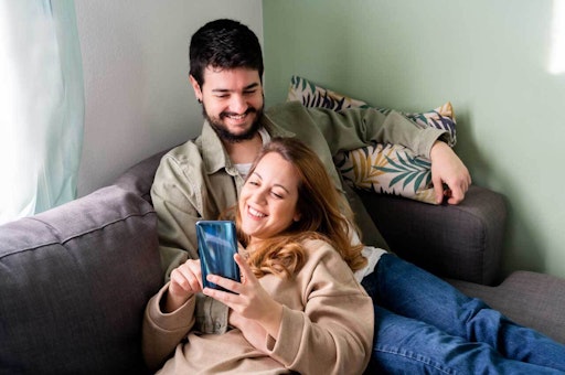 Couple cuddling on the couch, smiling and looking at phone