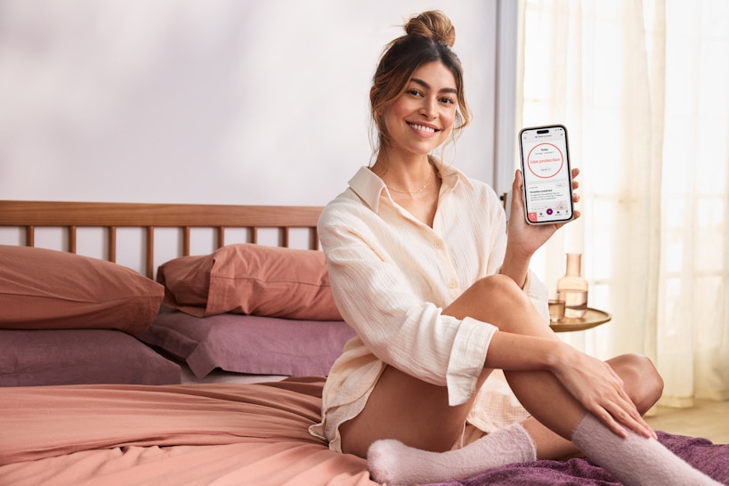 Women on bed holding phone showing Natural Cycles: use protection screen