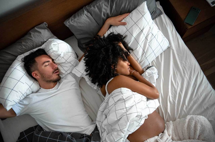 Couple asleep in bed partially covered by sheets