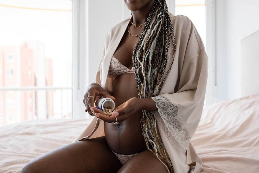 Pregnant woman sat on the bed taking supplements