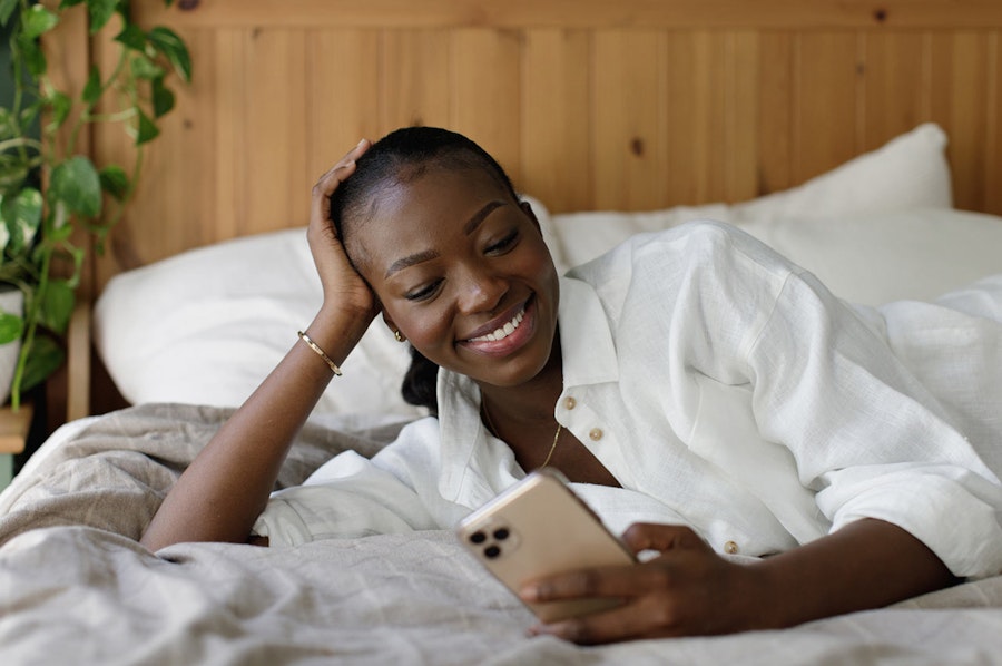 Woman smiling looking at her phone while laying in bed