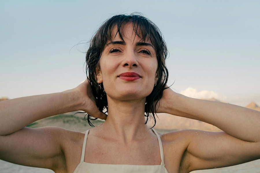 Person with bare arms standing with their back to the sun looking content