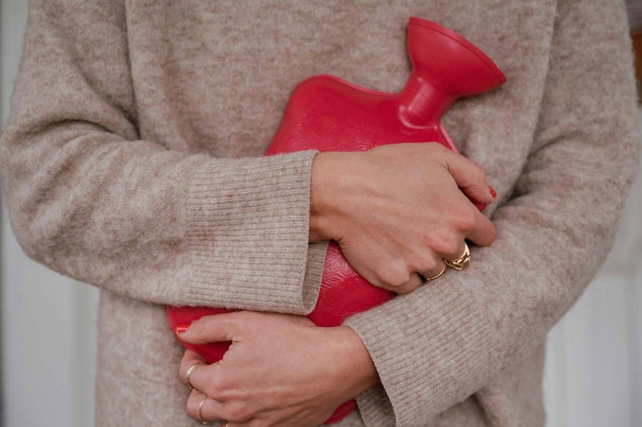 Woman in a cosy sweater holding hot water bottle to her stomach