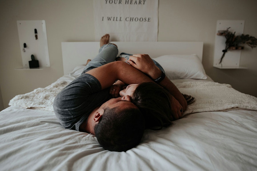 Clothed couple cuddling close on a bed above the covers