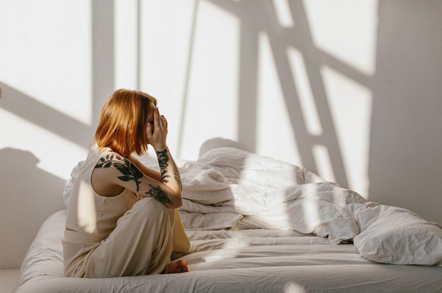 Red headed woman sitting on an unmade bed eith her head in her hands