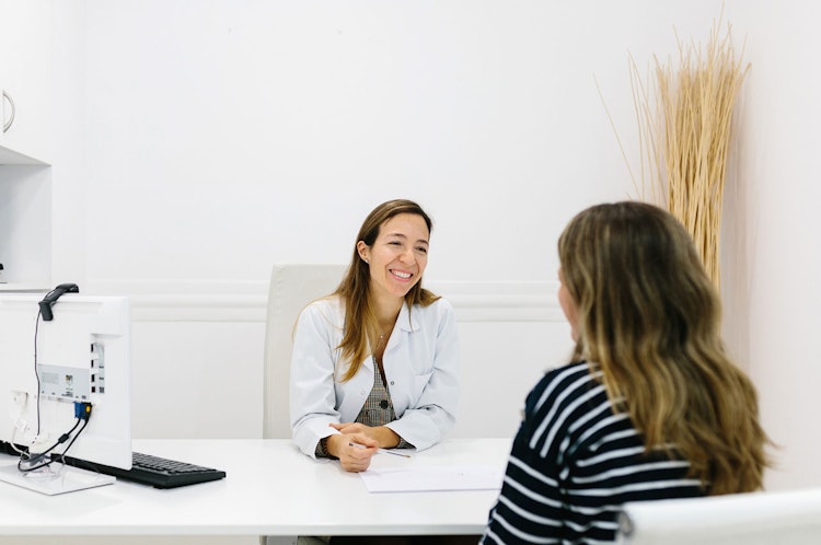 Kvinna som sitter hos en läkare och pratar medan läkaren ler