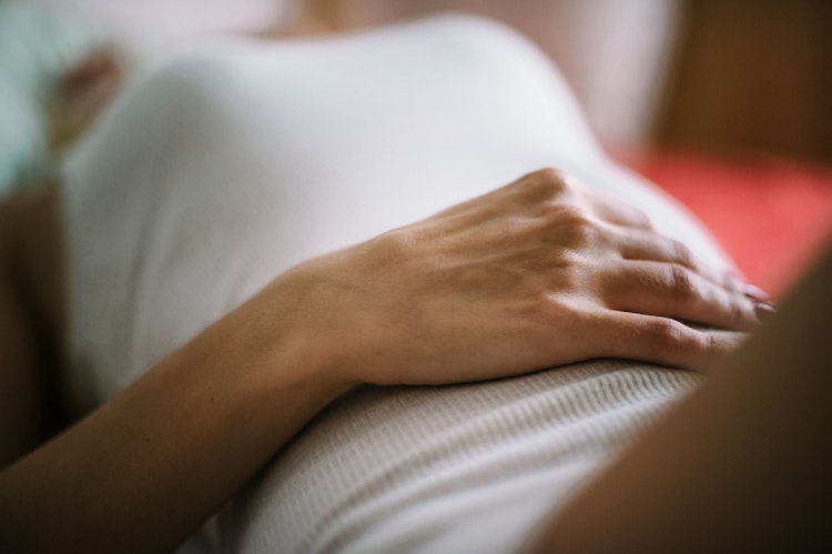 Woman holding her stomach lying on her back, illustrating feeling implantation cramps