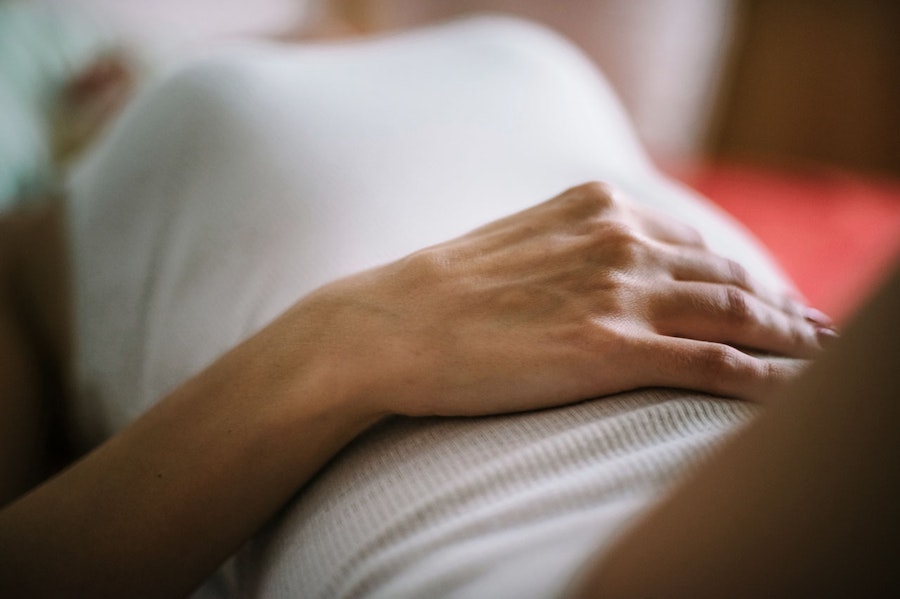Woman holding her stomach lying on her back, illustrating feeling implantation cramps