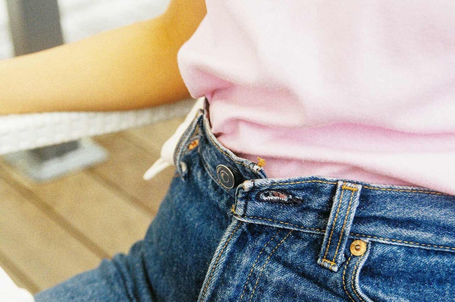 Woman sitting down with her jeans button open due to bloating