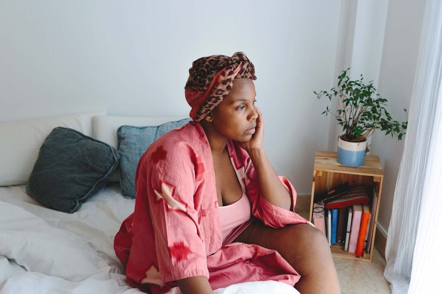Woman sat on the side of her bed looking tired
