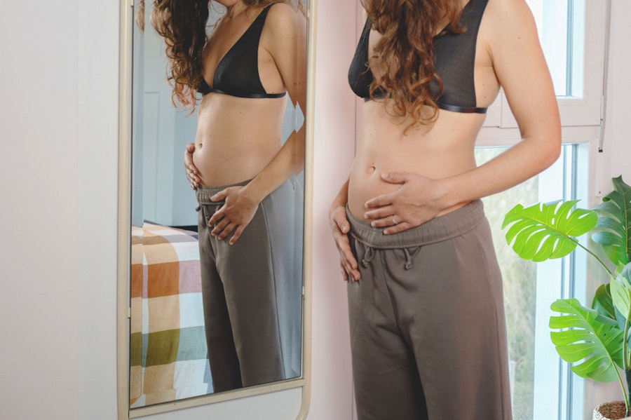 Woman looking at her small baby bump in the mirror