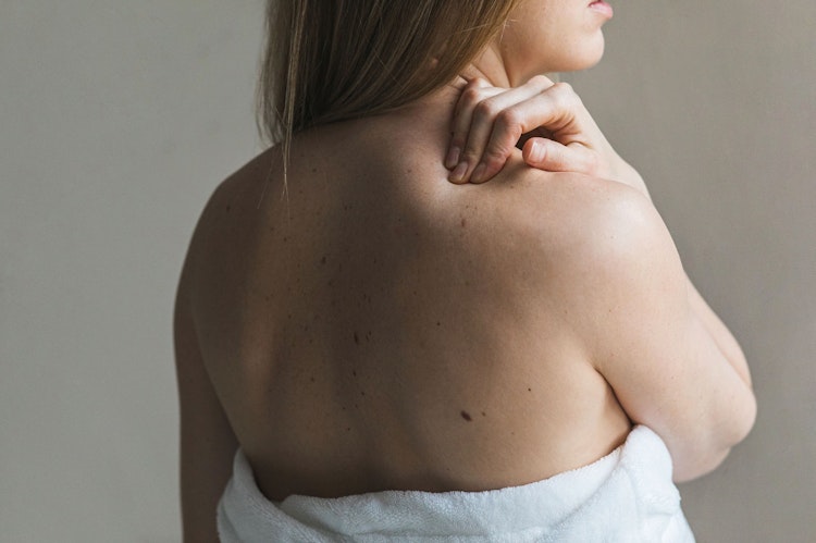 Woman wearing a towel, facing away with one hand on her shoulder