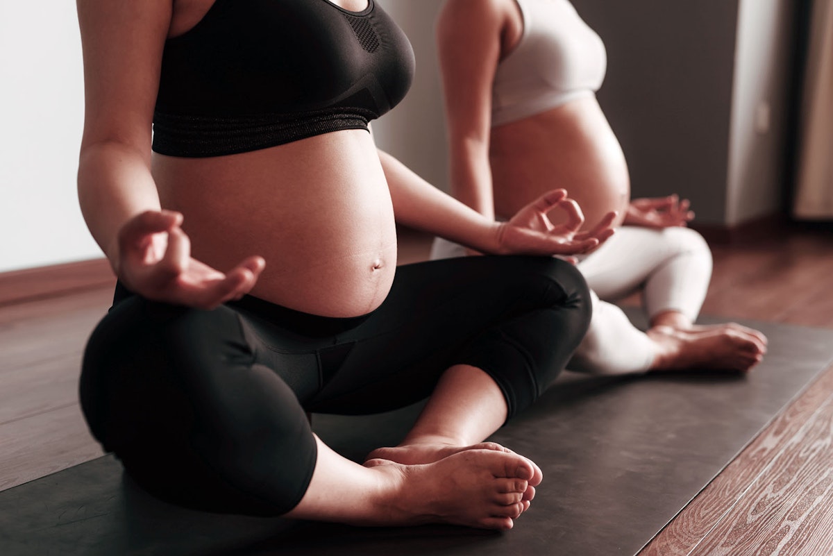 Two pregnant women sitting next to eachother on a yoga mat in lotus position