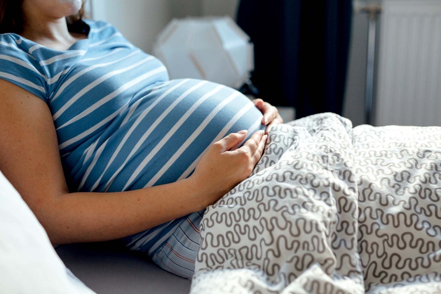 Pregnant woman lying in bed with her hands on her belly