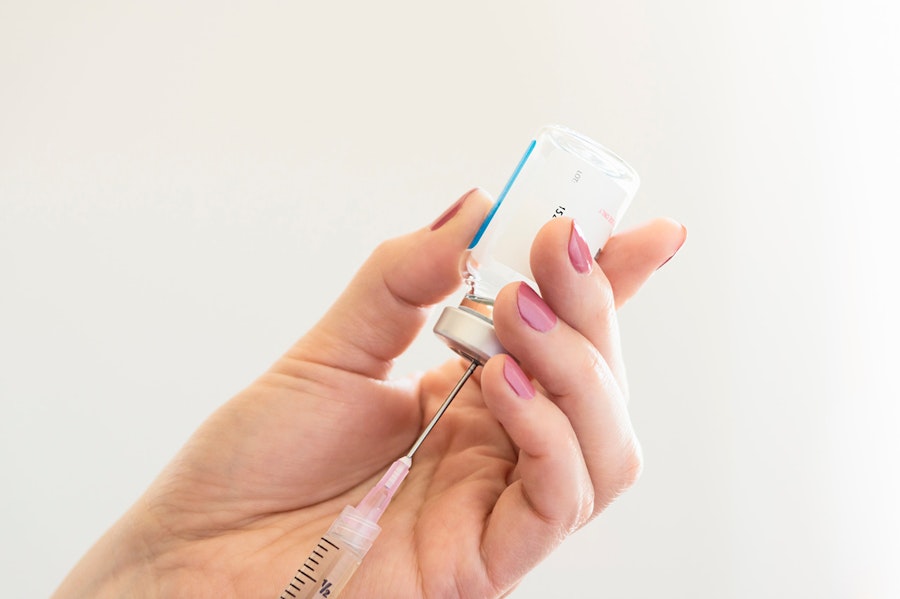 Needle, pulling solution from a vile, held in a hand wearing pink nail polish