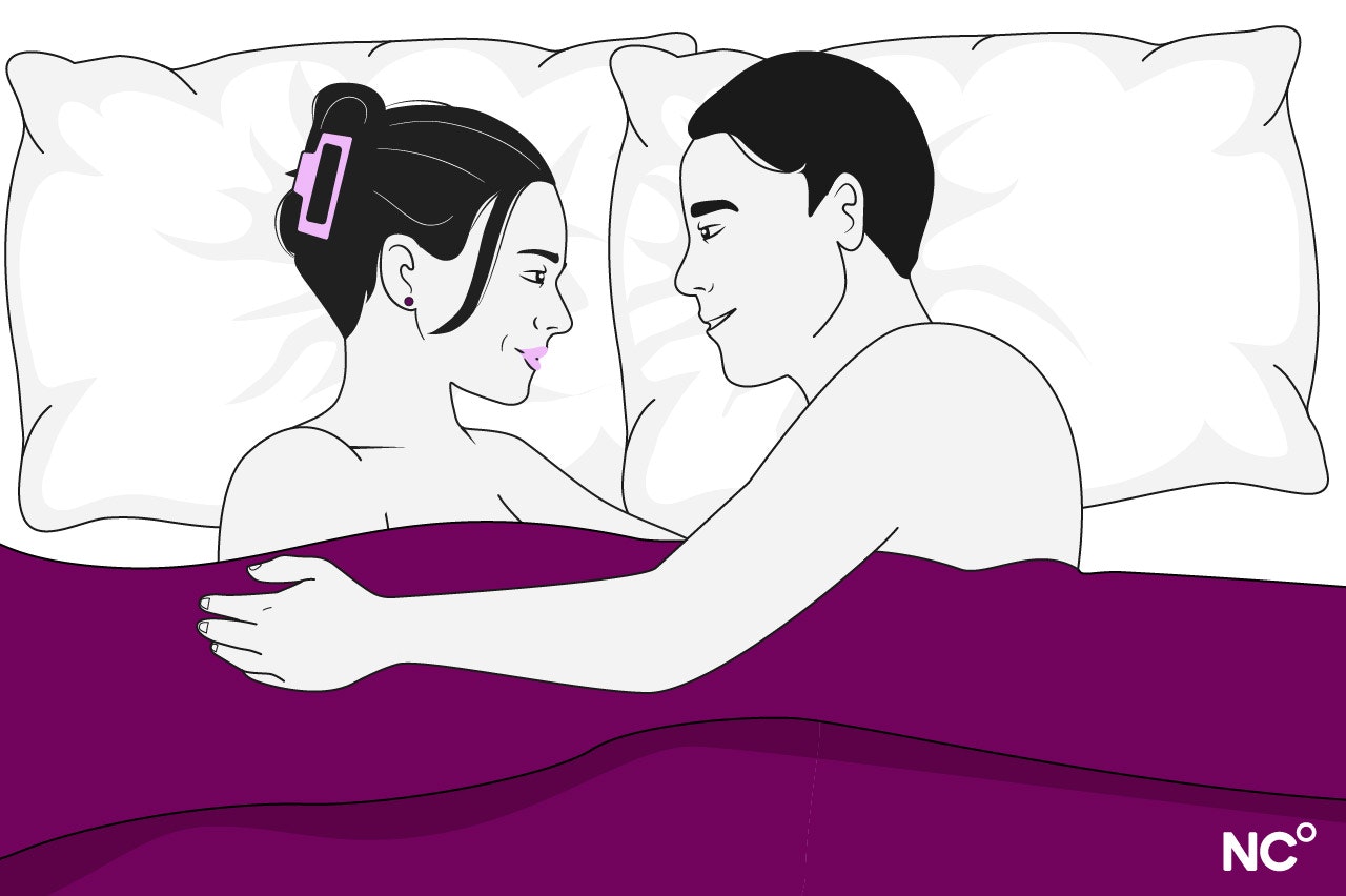 Illustration of a woman and man lying in bed under a purple cover facing eachother, embracing and smiling