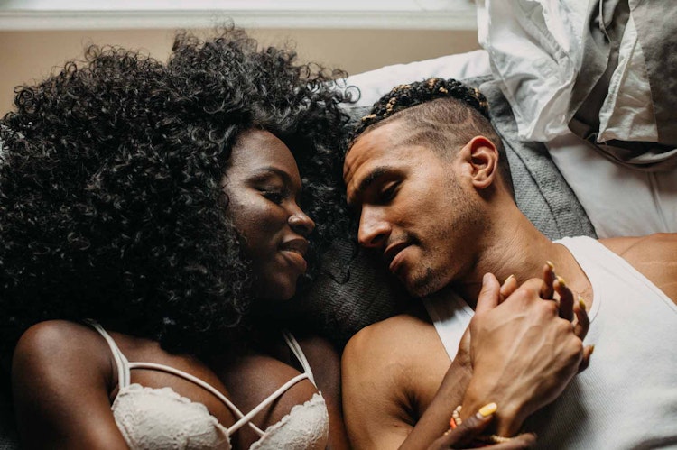 Couple in bed, holding hands and smiling with their eyes closed