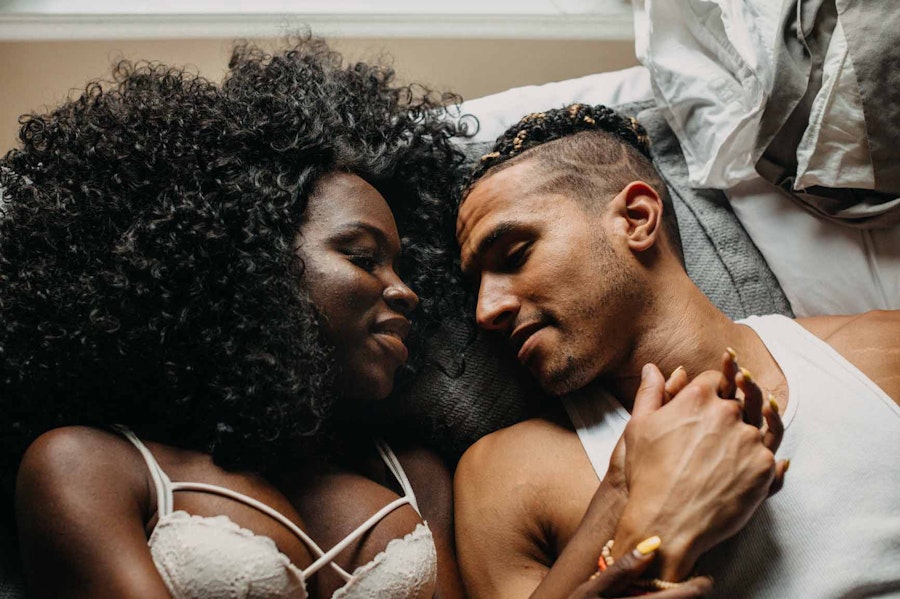 Couple in bed, holding hands and smiling with their eyes closed