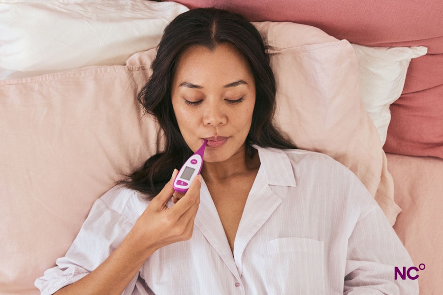 Woman in bed with a Natural Cycles thermometer in her mouth